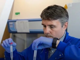 Professor Mark Cragg working in the lab. He is wearing a blue lab coat and holding two pipettes, one is each hand.