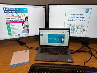 A desk setup with two large monitors and an open laptop. The monitors display information about the Experience Medicine Online course.