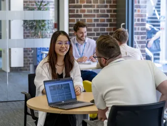 Professional services staff member meeting with a student at a table with a laptop in a university workspace.