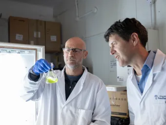 Professors Mark Moore and Tom Bibby examine a laboratory flask containing green algae culture.