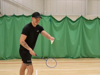 A player wearing a baseball cap and gym clothes about to serve at badminton