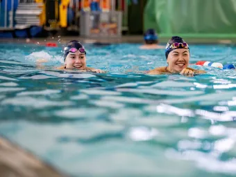 Two people wearing swimming hats and goggles swimming in a pool.