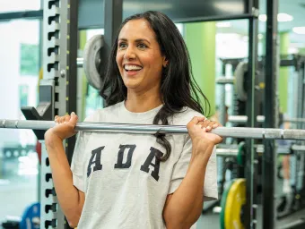 A smiling woman putting a bar weight back on the rest.