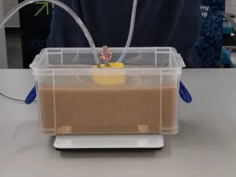 Demonstration model showing a foundation embedded in sand within a clear tank, used to illustrate offshore foundation engineering and seabed interactions
