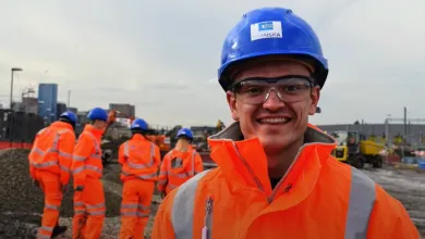 A group of engineering students in overalls and hard hats in an industrial setting