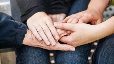 A close up of several overlapping hands holding each other, representing young, mid-life and older generations.