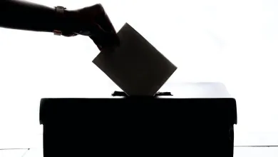 A silhouette of somebody's hand placing their vote into the polling booth box
