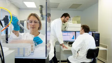 Researcher pipetting in a lab while two researchers talk in the background