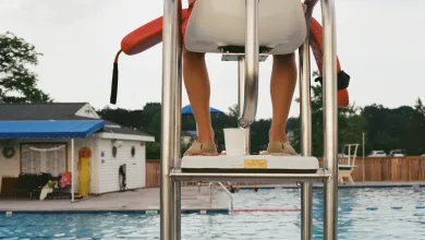 A lifeguard, seen from behind, keeps watch over on an outdoor swimming pool
