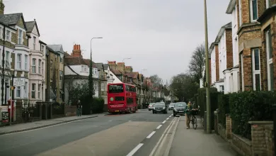 A road with a red bus, a cyclist pushing a bike, a pedestrian and cars