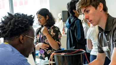 Four people in a medical training session, with one practicing a procedure on a manikin arm while others converse in the background, indicating a focus on skill development and collaboration.
