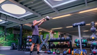 A man lifting a dumbell straightout in front of his body. There are lots of weights and equipment behind.