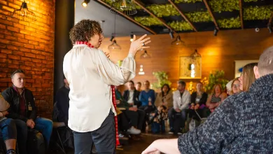 People are sitting around the edges of a room watching somebody giving a lively talk. 