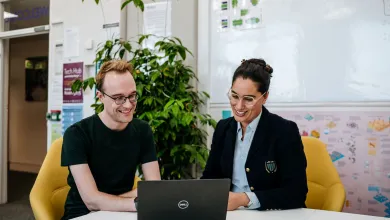 James Baker and Ammandeep K Mahal are in an office, smiling and looking at a laptop screen together.