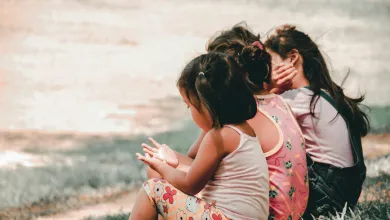 Three children sitting on grass, facing away, with colorful clothing.