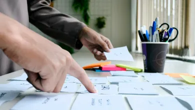 A finger points to a series of cards, another hand in the background gesticulates