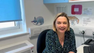 Professor Juliet Gray sitting at her desk, smiling. There are pangolin and leopard stickers on a white wall in the background. The window behind her is mostly covered by a light blue blind.