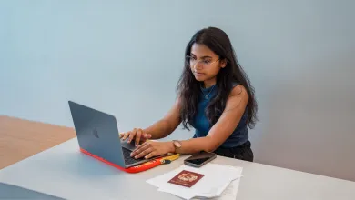 A student sat a desk with a laptop, mobile phone, passport and documents.