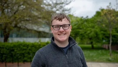 Smiling student wearing glasses standing outside the Physics building..
