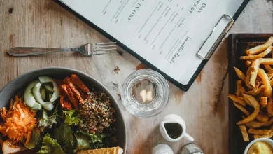 Table with a menu, bowl of salad and a plate of chips on it