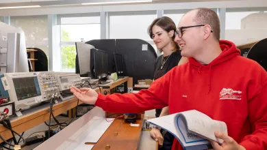 Two students in a physics laboratory using a variety of equipment, including a digital oscilloscope and a DDS function generator.