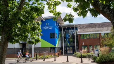 An exterior view of the main building at the Science Park. It is a sunny day and there are 2 cyclists on the road in front of the building.