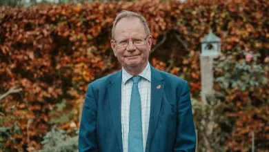 Portrait of Professor Stephen Holgate in a blue suit standing outdoors in front of autumn foliage.