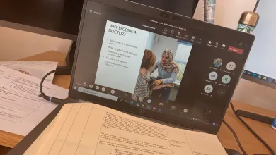 Laptop showing an online medical careers webinar with printed course materials on a desk.