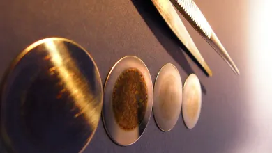 Four circular alpha spectrometry sample discs  displayed in a row, showing varying surface patterns and colouration for comparison.