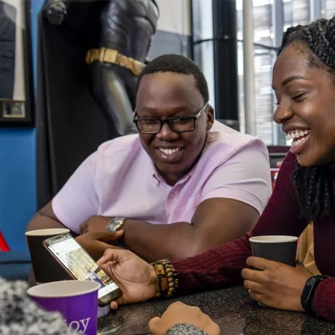 Students sitting around a table, smiling and looking at a phone