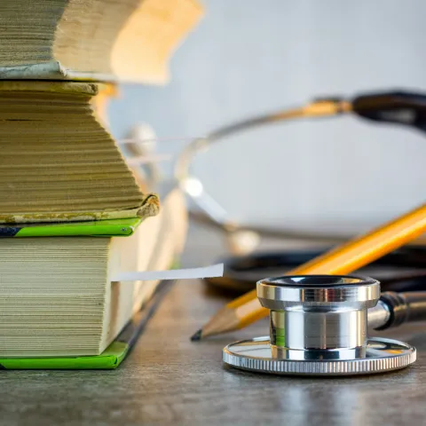 Stack of books, a stethoscope, and a yellow pencil on a wooden surface.