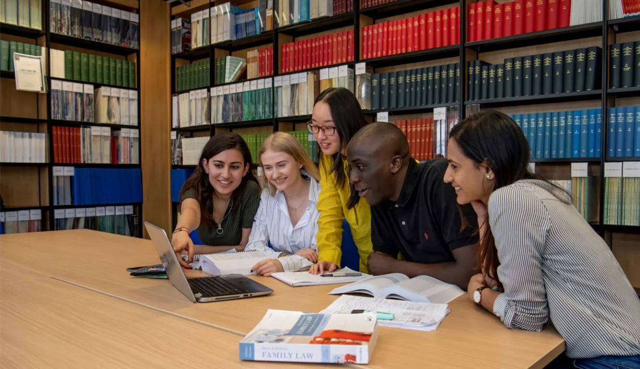 Students huddle around laptop in the library law collection