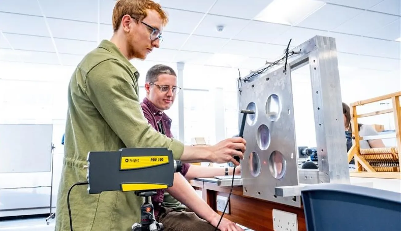 Two researchers conduct modal testing on a plate featuring circular dimples.