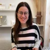 MSc Advanced Clinical Practice student, Chiara, sat in a cafe smiling for the photo. She's sat at a table with a croissant. 