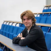 MSc Finance and Econometrics graduate, Stefan, sat in an empty lecture classroom smiling for a photo.