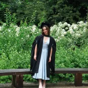 Isabelle, a BSc Pharmacology student, posing for a graduation photo in front of vibrant green foliage and white flowers. 