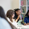 Psychology students sitting around a table. They are writing and mapping out work on a large piece of paper on the table. There are book shelves in the background.