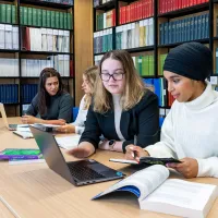 Four law students study together at a library table with laptops and open textbooks.