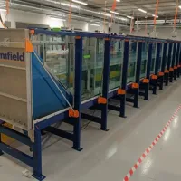 Long glass-sided wave tank in a laboratory, supported by a blue metal frame with orange fittings, and an Armfield wave generator positioned at one end.