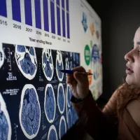 A person closely examining a large digital display of brain scan imagery.