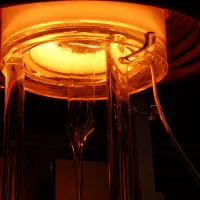 Glowing furnace with glass rods extending downward, emitting orange light.