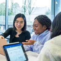 Students collaborating around a tablet displaying an academic diagram in a university study space.